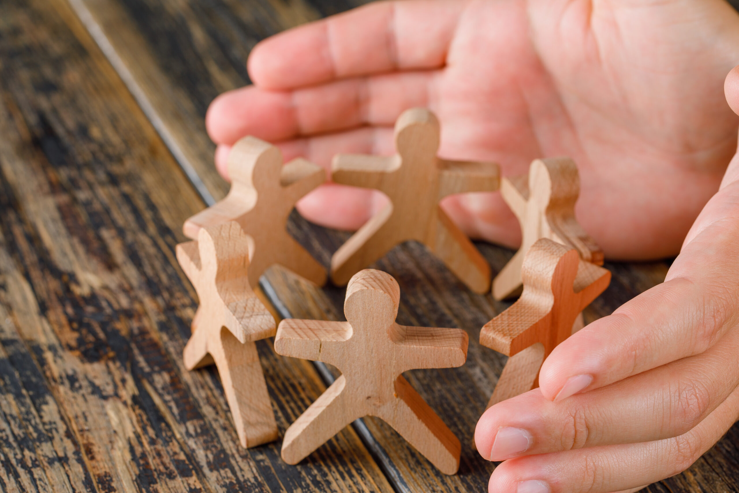 Business success concept on wooden background high angle view. hands protecting wooden figures of pe